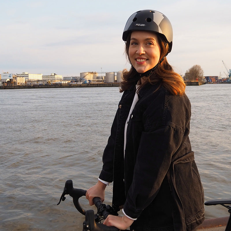 Woman standing by the Water with her Bike while wearing a Melon "Black Widow" Bicycle Helmet