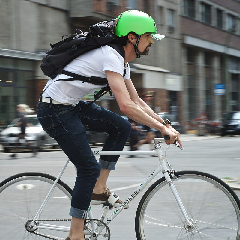Man wearing a backpack commuting through the streets of Berlin with a green Melon Bicycle Helmet