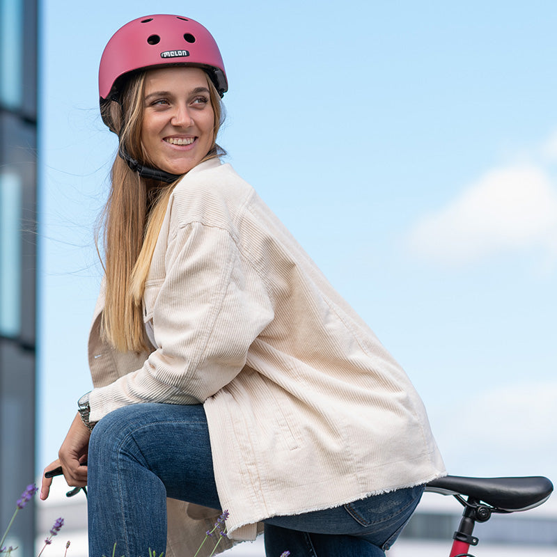 Woman smiling on her Bike while wearing a red Melon Helmet