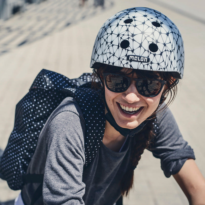Woman with a backpack on her Bicycle wearing a white Melon Synapse Helmet