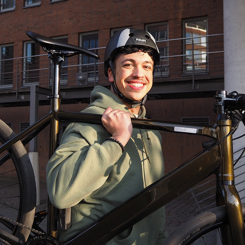 Man carrying a Bike while wearing a Melon "Black Widow" Bicycle Helmet