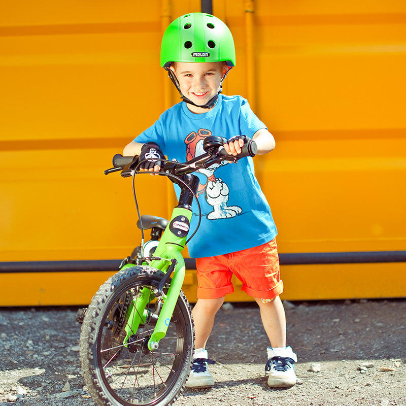 Boy with a green Bicycle standing in front of an orange wall wearing a green Melon Bicycle Helmet
