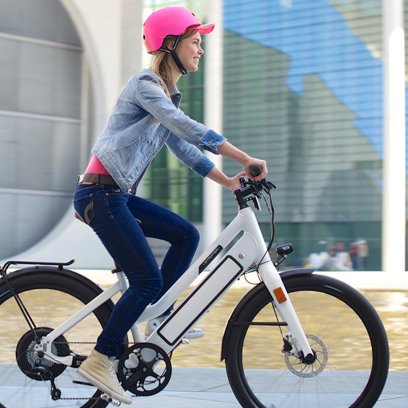 Young Woman riding her Pedelec through Berlin while wearing a Pink Melon Helmet