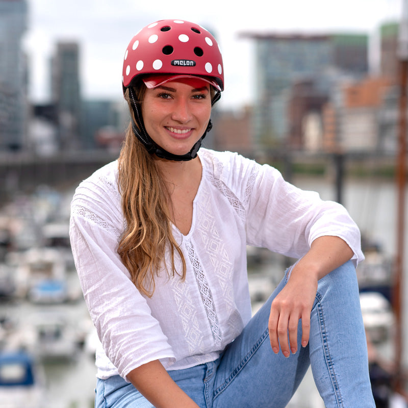 Woman in white Shirt and Blue Jeans sitting on a rock wearing a red Melon "Dotty White" Bicycle helmet in Düsseldorf