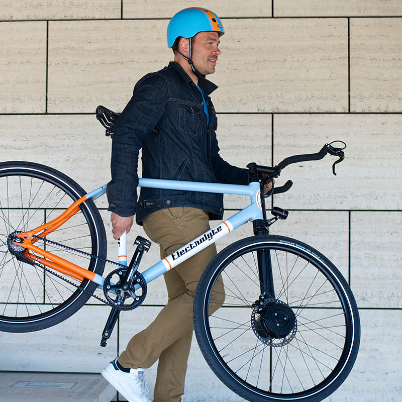 Man walking down stairs while holding his white bike wearing a Melon Urban Active Double Orange Blue Bicycle Helmet