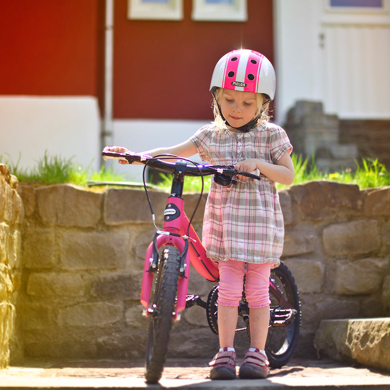 Girl and her Bike standing in front of a house wearing a Melon Double Pink White Bicycle Helmet
