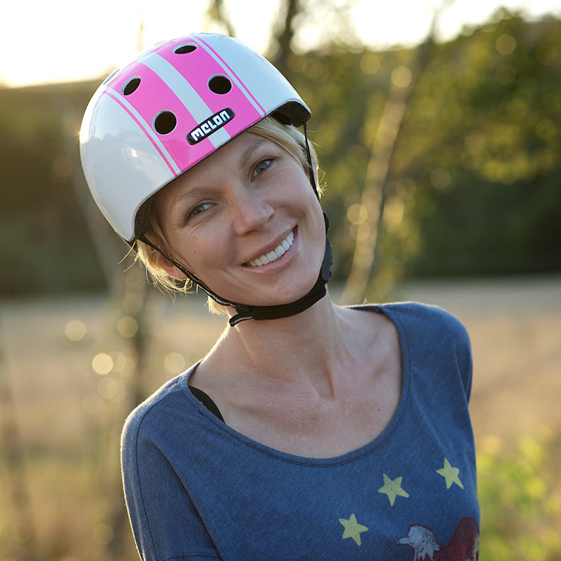 Woman standing in nature with her Melon Double Pink White Bicycle helmet smiling into the camera