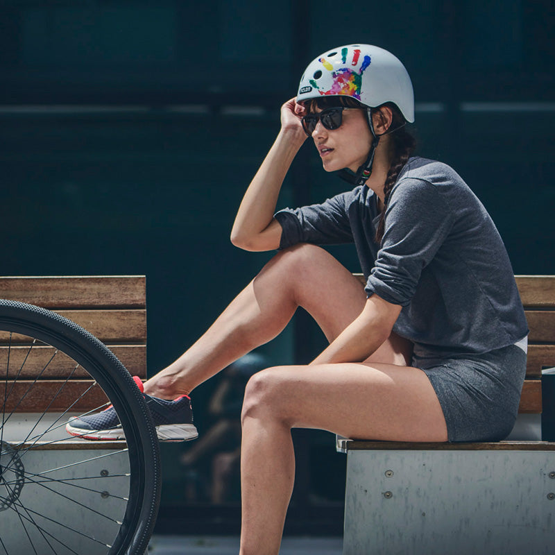 Woman sitting on a bench next to her Bicycle while wearing a Melon Handprint Helmet