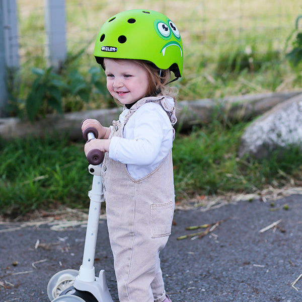 Little girl riding her Scooter while wearing a green Melon "Monster" Kids Bicycle Helmet