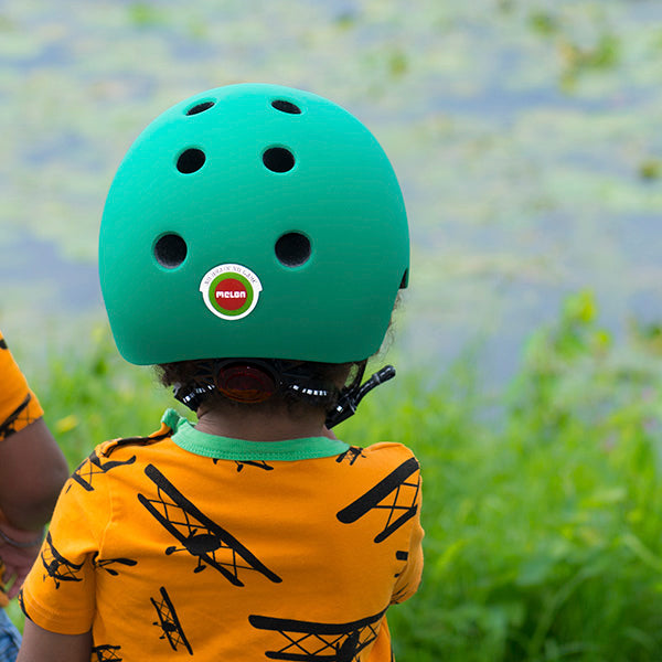 Toddler wearing a Melon Rainbow Green Baby Helmet by the lake