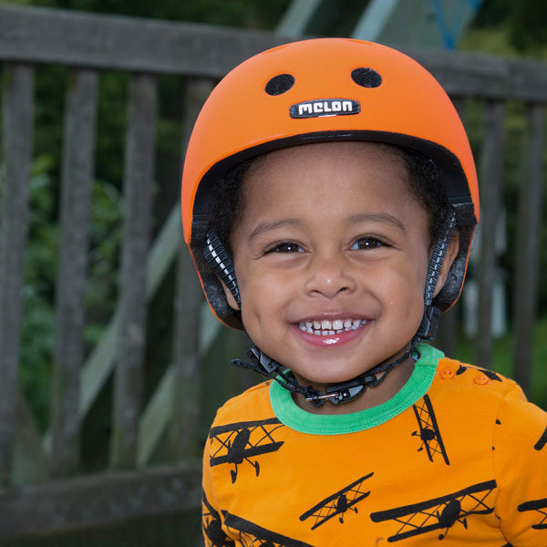 Toddler wearing an orange Melon Baby Bicycle Helmet smiling into the camera